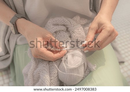 Fall and winter hobby. A skein of thread. Knitting from mohair yarn in hands of happy young woman. Soft and light colors. Positive emotions. Craft product. Warm knitted things. A pretty woman knits.