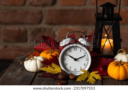 Fall winter time change concept. Autumn composition with retro alarm clock, bright yellow and red leaves, pumpkin, walnut, candle lantern. Brick wall on background. Cozy home atmosphere. Close-up