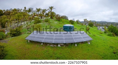 Fallbrook, California- Panorama of solar panels and cistern watertank on a sloped farm. Solar panels and water tank near the driveway of a mansion at the back on top of a mountain slope.
