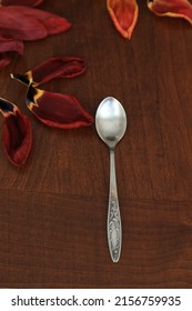 Fallen And Withered Red Tulip Petals And Cupronickel Teaspoon On A Natural Brown Wood Table Surface.