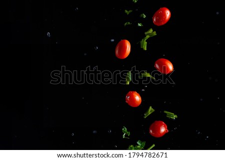Falling cherry tomatoes with parsley and onions, herbs, and drops of water, freeze in motion on a black background