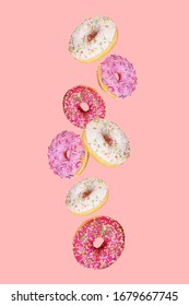 Falling doughnuts with multicolored glaze on trendy pink background. Donuts are traditional sweet pastries. Creative food trend. Levitating food. Vertical orientation.