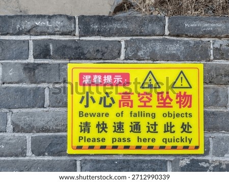 “Beware of falling objects” and “Please pass here quickly” Yellow warning sign in Chinese and English on the Great Wall of China 