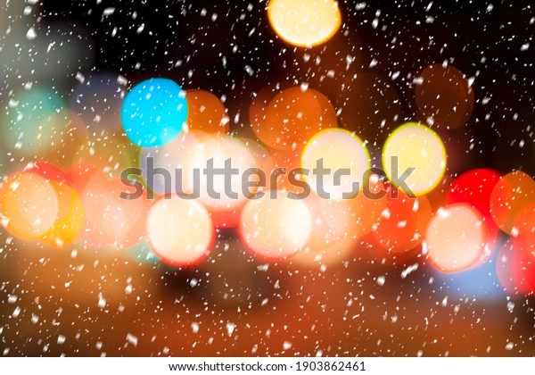 Falling snow against the background of blurry\
lights of headlights of cars and the night city. Winter snowfall\
concept. Abstract bright\
bokeh.