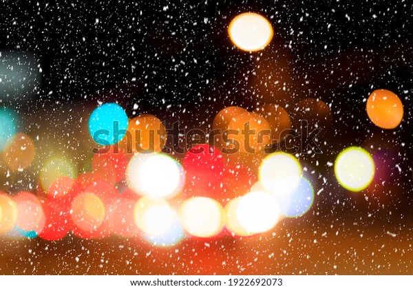 Falling snow against the background of blurry\
lights of headlights of cars and the night city. Winter snowfall\
concept. Abstract bright\
bokeh.