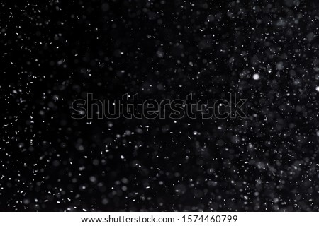 Falling  snow at night. Bokeh lights on black background, flying snowflakes in the air. Overlay texture. Snowstorm 