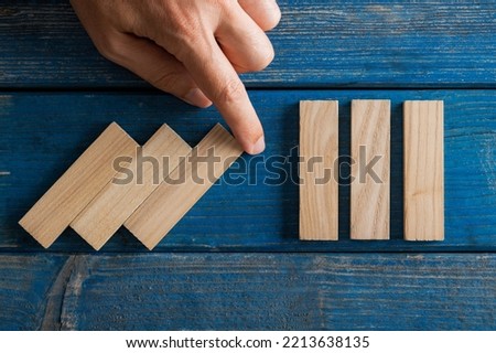 Falling wooden dominos being interrupted by male hand in a conceptual image of crisis management and proactive approach. Over wooden blue background. 