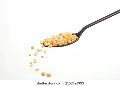 Falling Yellow Peas Grains From A Black Spoon On A White Background. Shallow Depth Of Field