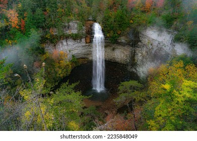 Falls Creek Falls is surrounded by vibrant fall colors and a misty morning haze. The waterfall cascades from a rocky cliff into a dark pool below. Photographed  at Falls Creek Falls State Park in TN. 