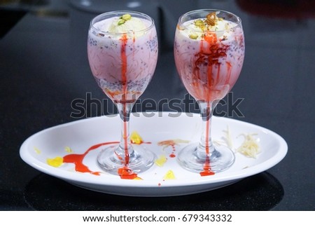 Falooda on a table mixed with rose syrup, vermicelli, sweet basil seeds, and pieces of jelly with milk, and topped off with a scoop of ice cream with dry nuts.