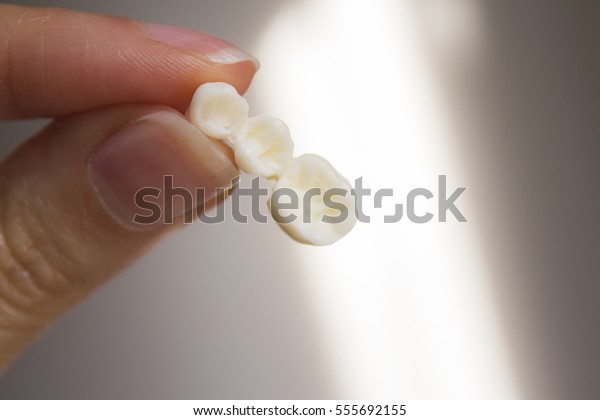 False teeth\
gripped by the hand of a\
woman\