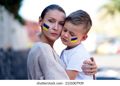 Families against war. Upset Ukrainian boy with his mother, with bue yellow flag on his face,  protesting war conflict. Evacuation of civilians. Freedom to Ukraine. Stop Russian aggression. Stop war 