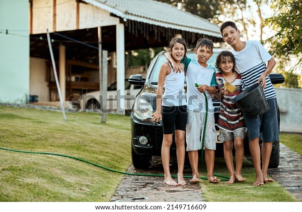 Families should always work together.\
Portrait of a group of young kids standing together and about to\
wash their parents car outside during the\
day.