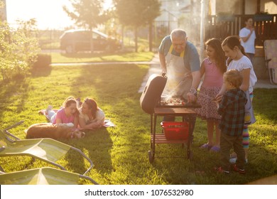 Familly Enjoying Picnic Some Are Grilling Some Are Laying On The Blanket With A Dog But Everyone Is Having Fun.