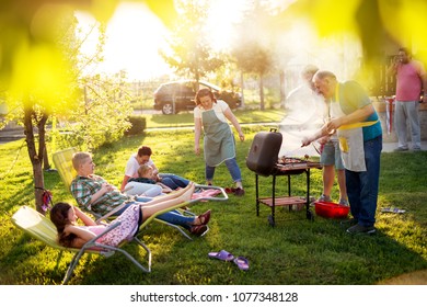 Familly Gathered And Is Having A Picnic And Grilling In Nature On A Beautiful Sunny Day.