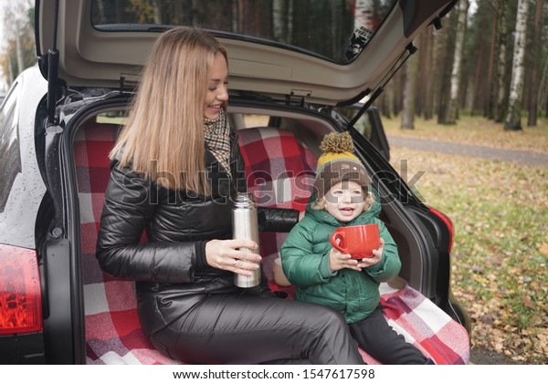 Family\
adventure - family on autumn camp. Young beauty mom and little\
child had picnic in back of car near the fall\
park