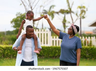 Family Of African American People With Young Little Daughter Walking On Green Grass Field While Enjoying Summer Garden Outside The House In The Neighborhood With Copy Space