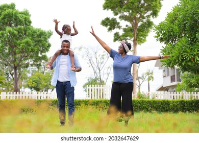 Family Of African American People With Young Little Daughter Walking On Green Grass Field While Enjoying Summer Garden Outside The House In The Neighborhood With Copy Space