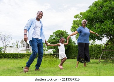 Family Of African American People With Young Little Daughter Walking On Green Grass Field While Enjoying Summer Garden Outside The House In The Neighborhood