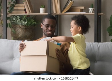 Family african father and little son opens unpack carton box sitting on sofa at home, satisfied clients received parcel. Delivery, shipping shipment, postal service, buying in internet stores concept