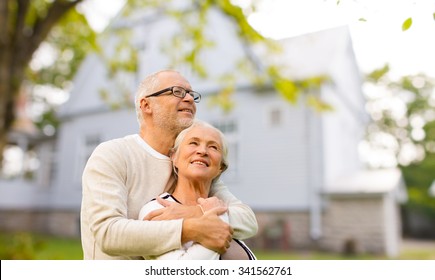 Family, Age, Home, Real Estate And People Concept - Happy Senior Couple Hugging Over Living House Background