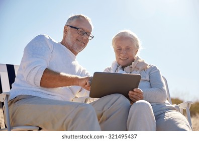 family, age, travel, tourism and people concept - happy senior couple with tablet pc computer resting in folding chairs on summer beach - Powered by Shutterstock