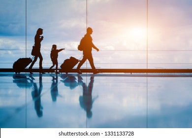 Family at airport travelling with young child and luggage walking to departure gate, girl pointing at airplanes through window, silhouette of people, abstract international air travel concept - Shutterstock ID 1331133728