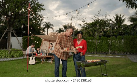 Family all together camp in garden, Old couple grill food for family member. Outdoor camping activity to relax with tasty meal and spend time with young generation cross generation gap. Divergence. - Powered by Shutterstock