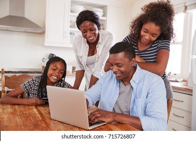 Family Around Kitchen Table Booking Vacation On Laptop Together