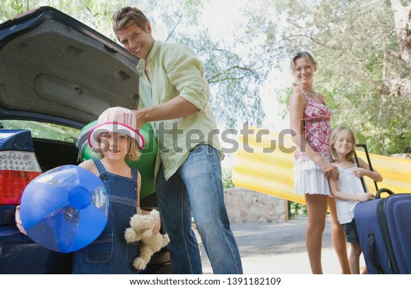 Family arriving at holiday villa with car luggage,\
smiling on summer vacation outdoors. Parents and children enjoying\
trip together with beach inflatables, tourists fun leisure\
recreation lifestyle. 