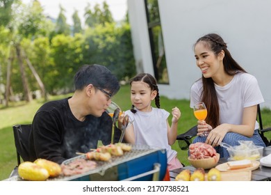 Family Asian Having Barbecue Party In Garden At Home. Smiling Parents Roast Beef With Daughter In Camping