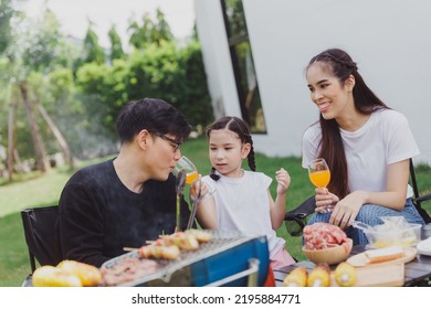 Family Asian Having Barbecue Party In Garden At Home. Smiling Parents Roast Beef With Daughter In Camping