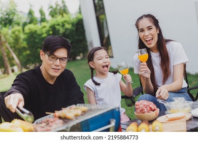 Family Asian Having Barbecue Party In Garden At Home. Smiling Parents Roast Beef With Daughter In Camping