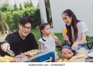 Family Asian Having Barbecue Party In Garden At Home. Smiling Parents Roast Beef With Daughter In Camping