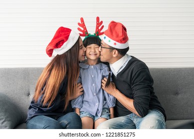 Family Asian Mother And Father With Daughter Happy And Kiss Together In Livingroom At Home In Christmas Day. 