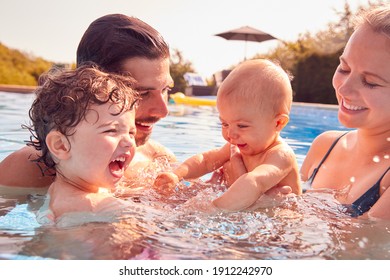 Family With Baby Daughter Having Fun On Summer Vacation Splashing In Outdoor Swimming Pool