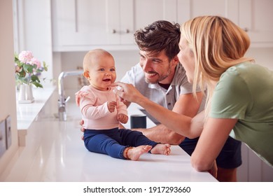 Family With Baby Daughter Having Fun Playing Game Sitting In Kitchen Together - Powered by Shutterstock