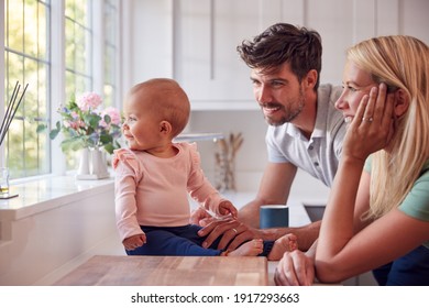 Family With Baby Daughter Having Fun Playing Game Sitting In Kitchen Together