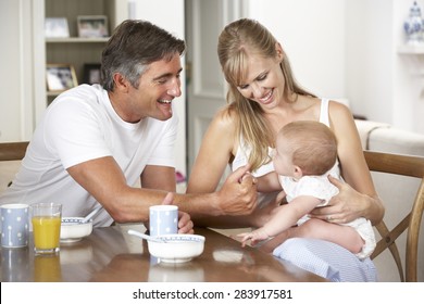 Family With Baby Having Breakfast In Kitchen Together