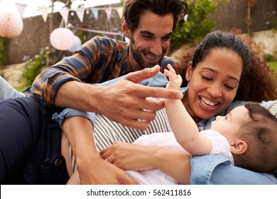 Family With Baby Playing On Rug In Garden Together