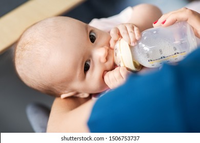 Family, Babyhood And People Concept - Close Up Of Mother Feeding Baby With Milk Formula From Bottle