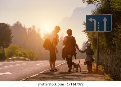 Family Backpackers Goes On Mountain Road At Sunset