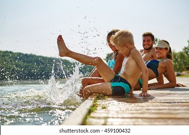 Family Bathing And Splashing Water With Their Foot At A Lake In Summer