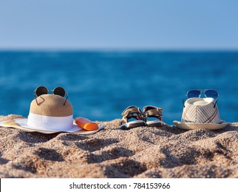 Family Beach Accessories. Fatherâ??s Sunhat, Motherâ??s Bonnet Hat, Sandals Of A Child And Bottle Of Sunscreen Against The Sea.