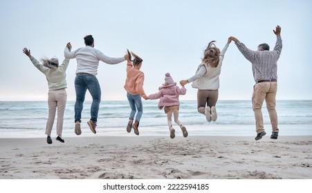 Family At The Beach, Adventure And Jump, Generations Love And Care While Holding Hands And Fun By The Ocean. Big Family Travel, Parents With Grandparents And Children Together And Freedom At Sea.