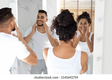 Family Beauty Care. Young Arab Spouses Using Moisturising Face Cream While Standing Near Mirror In Bathroom, Happy Millennial Middle Eastern Couple Smiling To Their Reflection, Selective Focus - Powered by Shutterstock