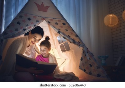 Family Bedtime. Mom And Child Daughter Are Reading A Book In Tent. Pretty Young Mother And Lovely Girl Having Fun In Children Room.