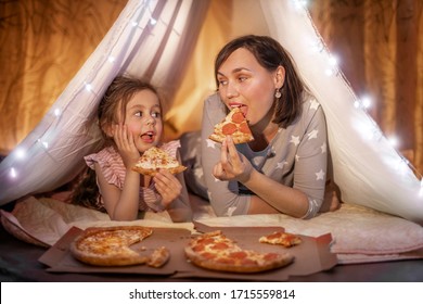 Family Bedtime. Mom And Daughter Eat Pizza In A Tent. Pretty Young Mother And Lovely Girl Having Fun In Children Room.