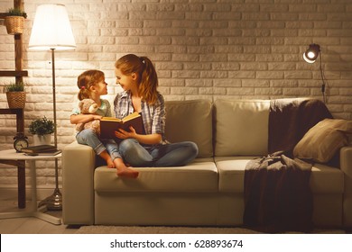 Family Before Going To Bed Mother Reads To Her Child Daughter Book Near A Lamp In The Evening
