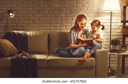 Family before going to bed mother reads to her child daughter book near a lamp in the evening